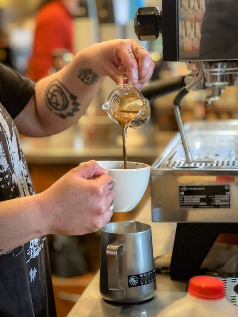 Barista pouring espresso shots into a mug.